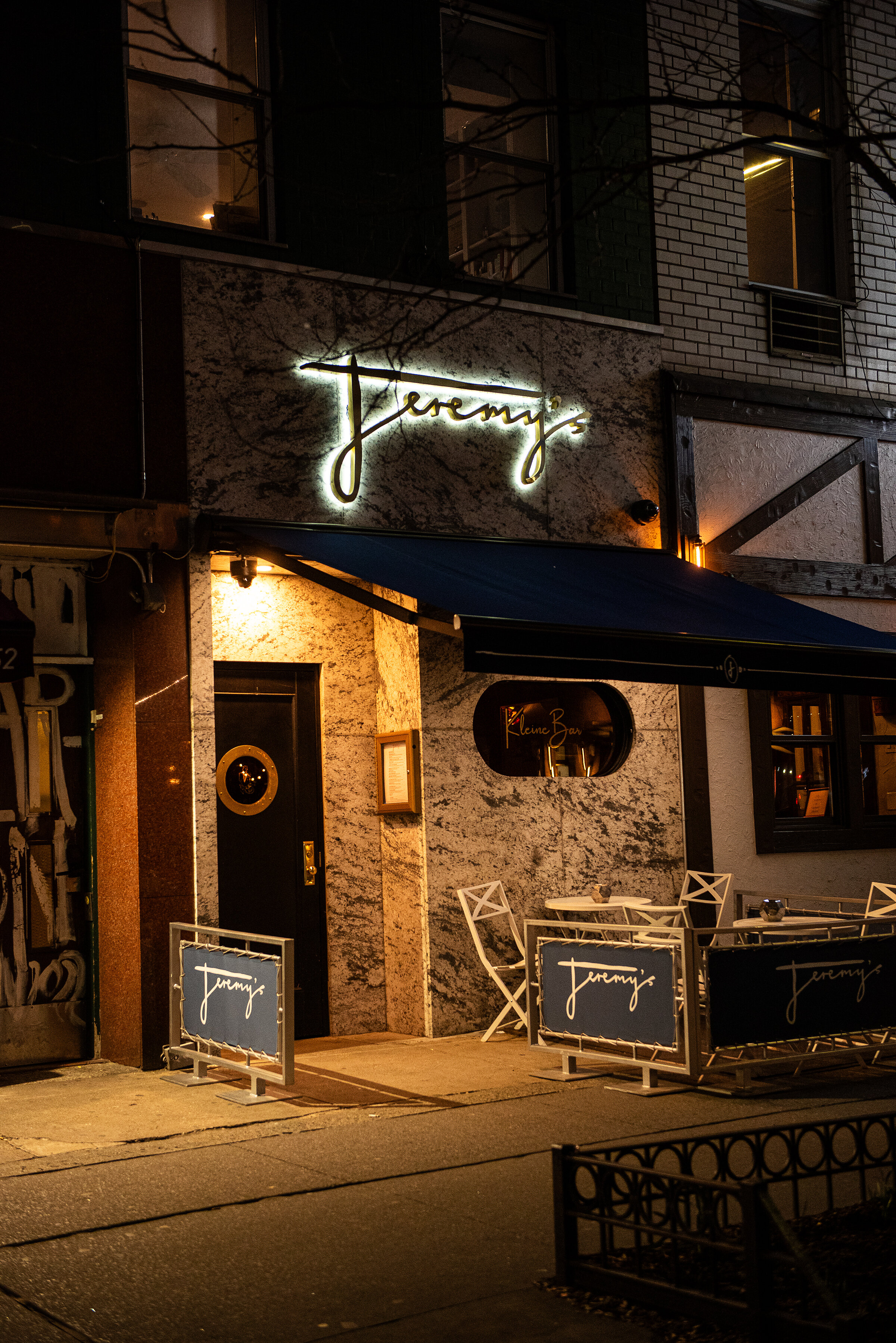 Jeremy's storefront at night — neon sign, marble facade, sidewalk seating